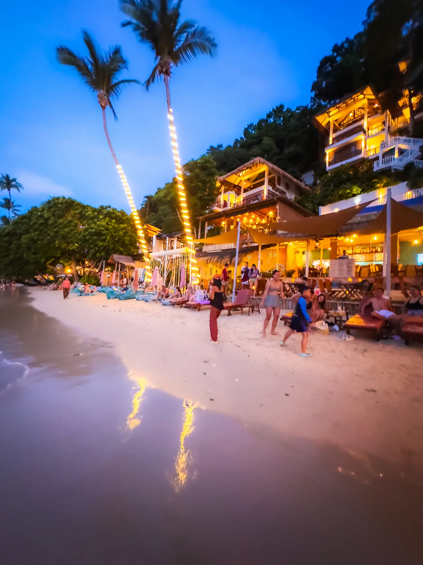 A scenic beachfront view of the Maremegmeg Beach Club resort in El Nido, Palawan. The resort features modern design, an infinity pool, and comfortable outdoor seating, all situated directly on the white sand of Maremegmeg Beach with a panoramic view of Bacuit Bay.