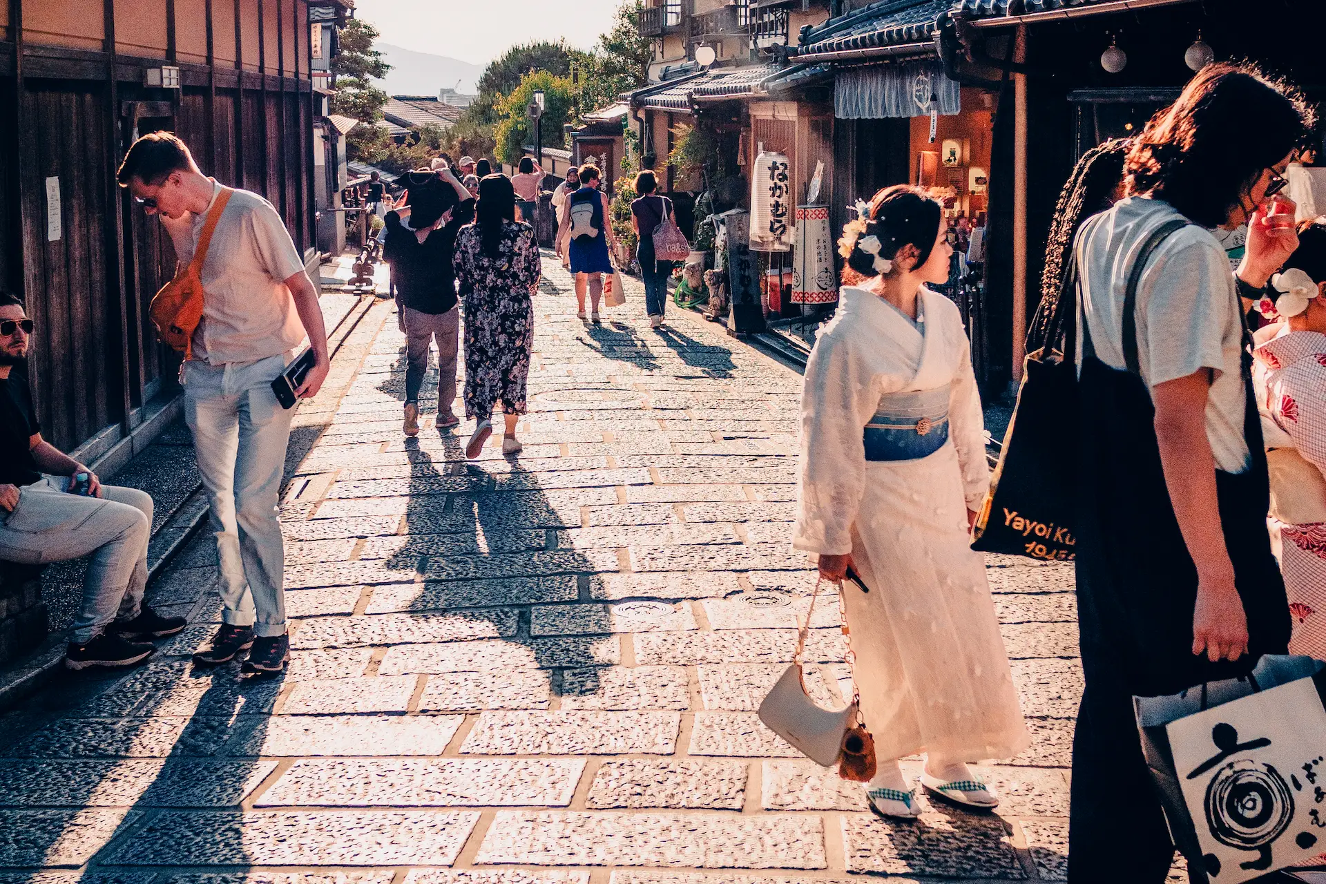 People walking down the historic stone-paved Sannenzaka slope in Kyoto during a Japan travel itinerary, with golden afternoon light reflecting on the pathway.