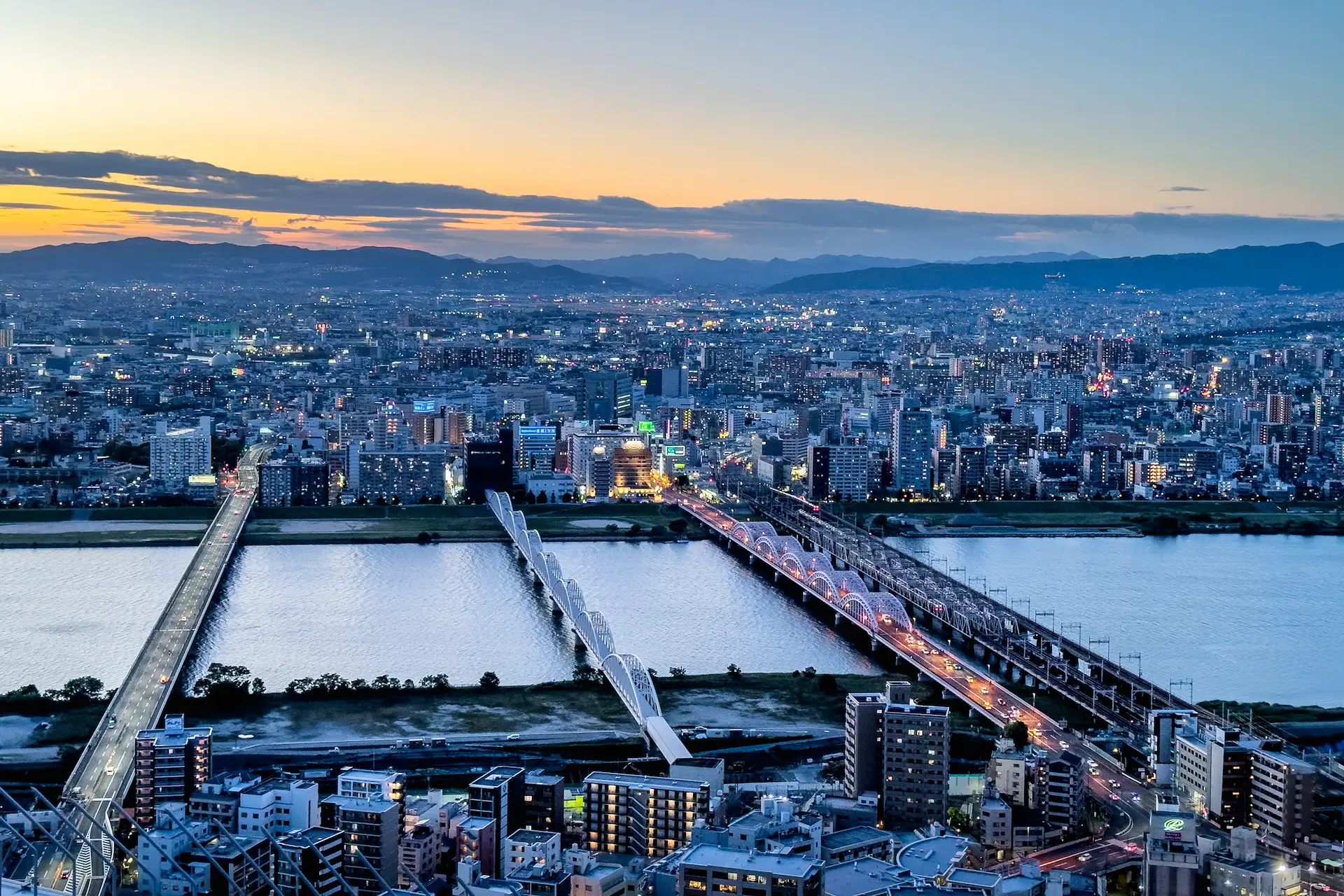 An aerial view of the Osaka city skyline and bridges crossing the Yodo River at sunset during a Japan travel itinerary.